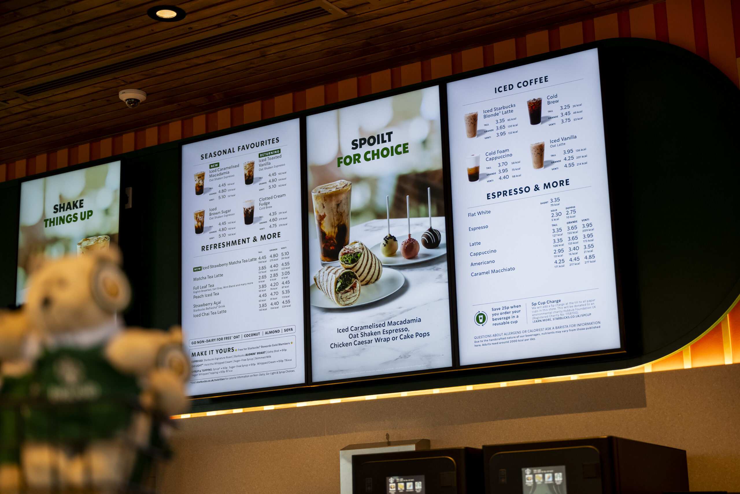 Starbucks Digital Media Screen hanging in a Starbucks. Small Starbucks Bear is in the foreground but its out of focus.